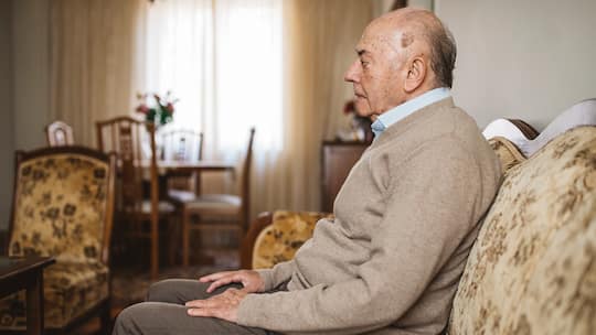 Alter Mann sitzt in seiner Wohnung auf dem Sofa