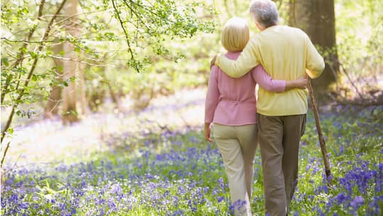 Ein älteres Paar spaziert Arm in Arm im Wald.