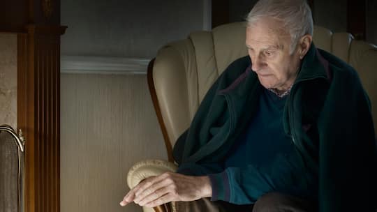 Ein alter Mann sitzt in seiner Wohnung und friert