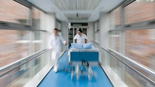 Arzt und Pflegefachkraft schieben Spitalbett durch Gang