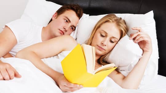 Ein junges Päärchen liegt im Bett. Sie liest.