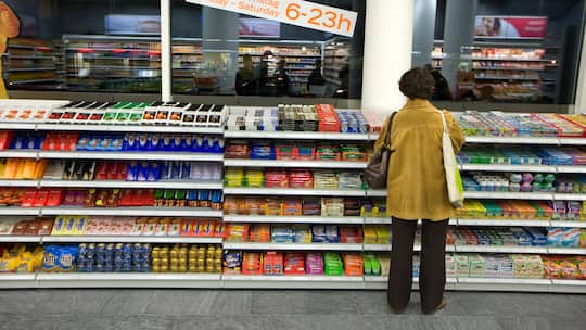 Eine Frau steht vor einem Verkaufsregal mit Schokoriegeln in einem Coop-Pronto. Die Preise der beiden grössten Detailhändler Coop und Migros sind oftmals identisch. Schreiben sich die beiden Riesen bei den Preisen etwa ab?
