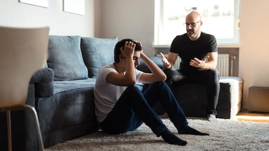 Ein Vater und sein Sohn führen im Wohnzimmer ein Gespräch, doch der Sohn scheint daran desinteressiert zu sein und fasst sich mit den Händen an den Kopf, als Worte er die Worte seines Vaters nicht anhören.