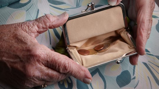 Eine ältere Frau öffnet ihre Geldbörse, in der sich nur wenige Münzen befinden.