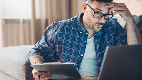 Ein junger Mann sitzt mit sorgenvoller Miene vor seinem Laptop.