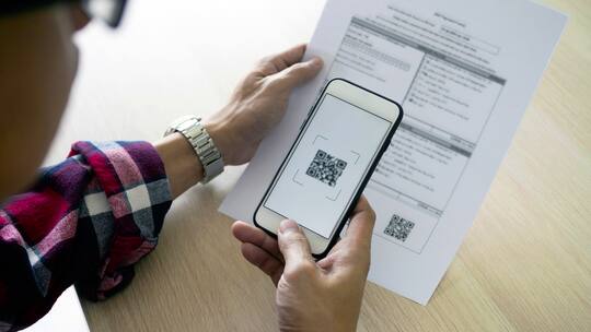 Ein junger Mann hat seine Handykamera auf einen QR-Code gerichtet, um diesen zu scannen.