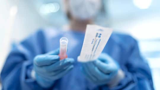 Person in Schutzkleidung hält Corona-Testkit