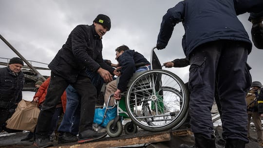 Mann in Rollstuhl wird bei der Überquerung des Flusses in der ukrainischen Stadt Irpin geholfen