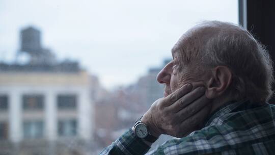 Älterer Mann blickt nachdenklich aus dem Fenster