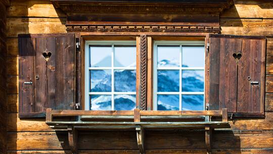 Bergpanorama spiegelt sich in Fenstern eines alten Hauses