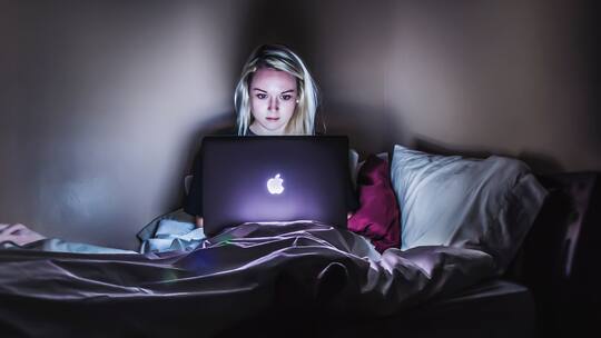 Frau mit Macbook auf dem Bett