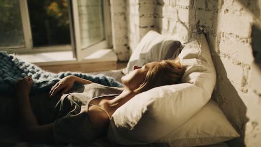 Frau schläft bei offenem Fenster im Bett