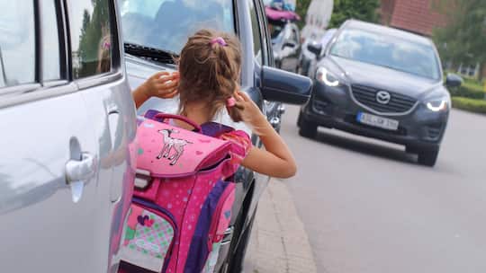Zwischen parkierenden Autos stehende Schülerin erblickt herannahendes Auto