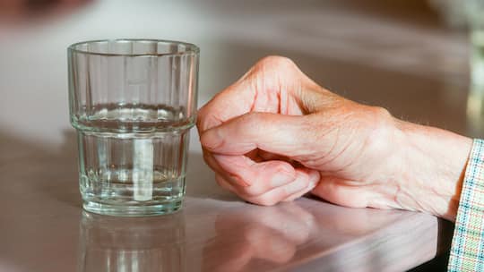 Hand der Bewohnerin einer Seniorenresidenz liegt neben einem Wasserglas