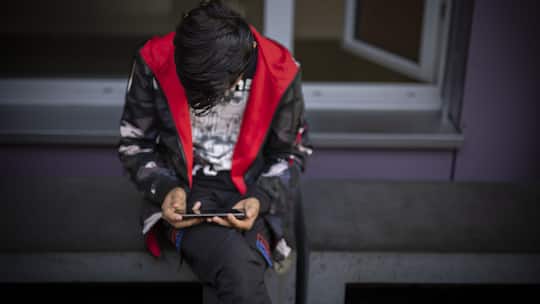 Ein Mann sitzt auf einer Bank und benutzt sein Mobiletelefon, aufgenommen waehrend eines Medienrundgans im Bundesasylzentrum Zuerich, am Donnerstag, 27. Oktober 2022 in Zuerich. (KEYSTONE/Michael Buholzer)