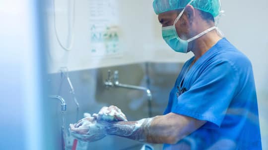 2E4JEPP Male surgeon in surgical cap using smart phone at hospital