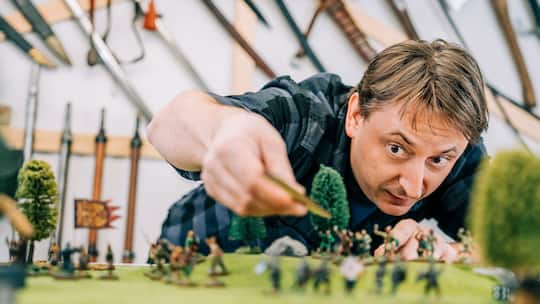Tabletop-Spieler Simon Künzle denkt über den nächsten Zug nach. Er beugt sich über eine künstliche Landschaft mit Spielfiguren.