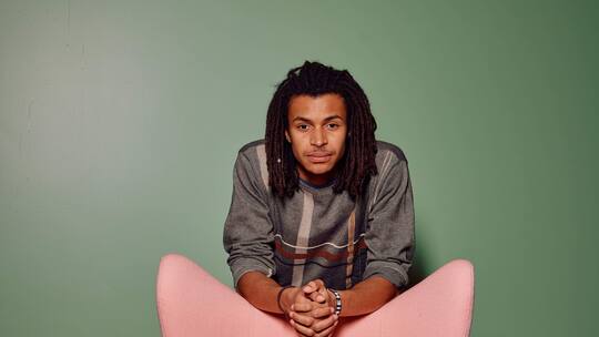 Regisseur Damien Hauser hat einen Film über eine Vergewaltigung gedreht. Er steht hinter einem rosa Sessel, vor einer grünen Wand.