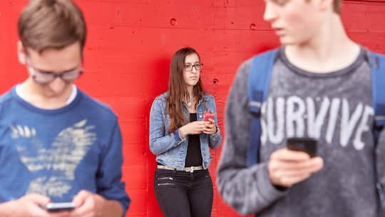 Jugendliche schaut betroffen, während zwei Jungs über verbreitete Inhalte auf dem Handy sprechen.