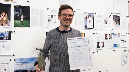 Yves Demuth posiert mit dem Prix Transparence 2022, den er für seine Recherche zu weiblichen Teenagern, die nach dem zweiten Weltkrieg Zwangsarbeit leisten mussten, gewonnen hat. Catherine Duttweiler hat ihn zum Thema Energiewende gewonnen.