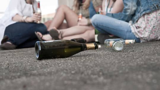 Jugendliche mit einer leeren Proseccoflasche auf dem Boden sitzend