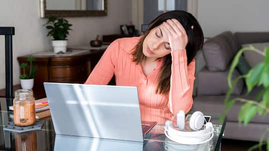 Eine junge Frau sitzt an einem Glastisch mit sorgenvoller Miene, vor ihr ist ein Laptop aufgeklappt.