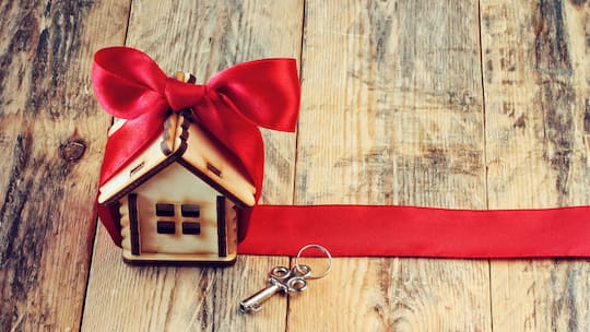 Ein kleines Holzhaus ist mit einer roten Schleife eingepackt und liegt neben einem Schlüssel auf einem Holztisch