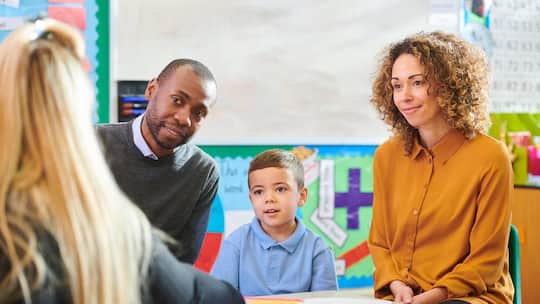 Elternpaar mit Kind vor der Lehrerin - Eine konstruktive Zusammenarbeit zwischen Schule und Eltern kommt Kindern und Jugendlichen zugute. Zwei Fachpersonen erklären, wie die Kooperation gelingt