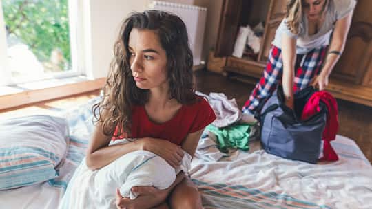 Frau sitzt nachdenklich auf Bett