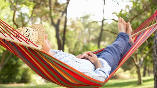Rentner liegt in Hängematte auf grüner Wiese.