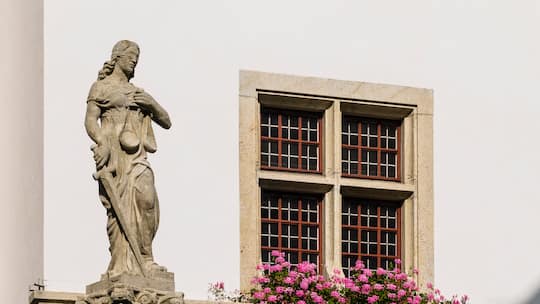 Rathausbrunnen mit Justitia in Brugg, Aargau. Im Hintergrund ein Haus mit einem Fenster mit Geranien
