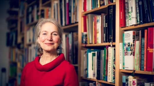 Die Ernährungswissenschaftlerin Christine Brombach trägt einen roten Pullover, steht vor einer Bücherwand und lächelt.