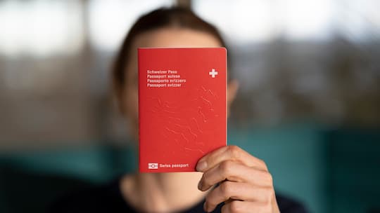 Eine Person hält einen Schweizer Pass hoch.