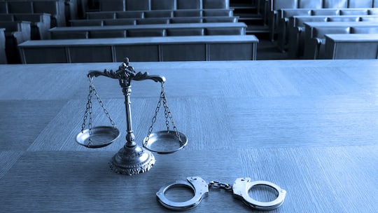 In einem abgedunkelten Verhörsaal steht ein grosser Tisch, auf dem eine Waage und Handschellen liegen. So funktioniert in der Schweiz das «vereinfachte Verfahren» bei Gerichtsprozessen.