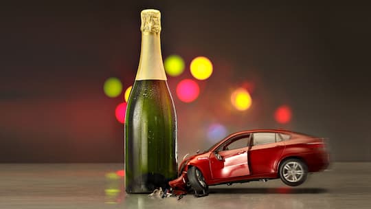 Symbolisches Bild in welchem ein Spielzeugauto in eine Sektflasche kracht