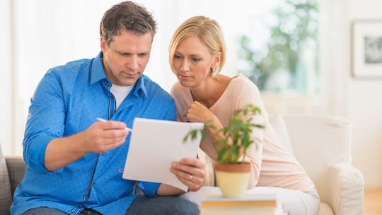 Ein Paar sitzt auf einem Sofa im Wohnzimmer, der Mann hält einen Vertrag in seinen Händen und schaut sich diesen zusammen mit seiner Partnerin an.