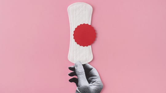 Binde mit rotem Punkt aus Papier wird von schwarzweisser Hand gehalten. Alle 28 Tage laufen Frauen am Arbeitsplatz auf Sparflamme. Die Mens! Wer auf den Zyklus achtet, kann die Hormonkapriolen nutzen.