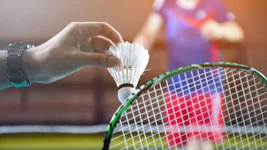 Men single badminton player holds racket and white cream shuttlecock in front of the net before serving it to another side of the court, soft and selective focus.2213567439