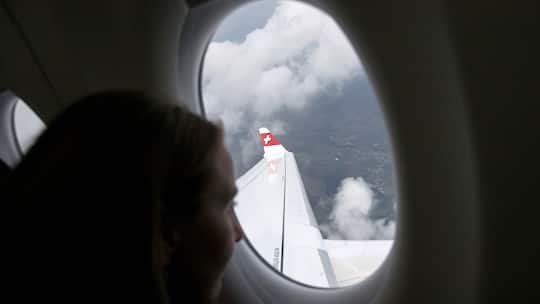 Swiss: Passagierin blickt aus Fenster auf Flugzeug-Tragfläche. Ein und derselbe Flug kostet einmal Fr. 718.52, ein anderes Mal Fr. 92.55. Günstig fliegt nur, wer Hin- und Rückflug bucht.