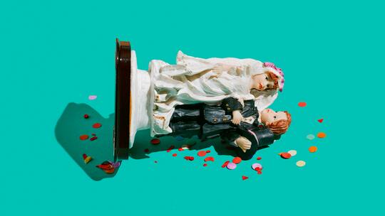 Eine Tortenfigur mit einem Ehepaar liegt umgekippt auf einer grünen Fläche.