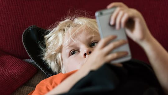 Ein junger Teenager-Junge liegt auf dem Sofa und hat ein Handy in der Hand