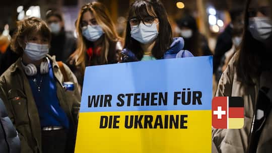 Junge Demonstrierende halten ein Plakat in den Farben der ukrainischen Flagge, auf der geschrieben steht «Wir stehen für die Ukraine».