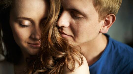 Paar, das eng umschlungen dasteht. Er riecht an ihren Haaren.