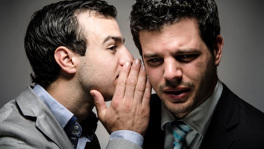 Ein Mann flüstert einem anderen Mann etwas ins Ohr