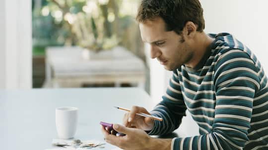 Junger Mann tippt etwas auf seinen Taschenrechner ein.