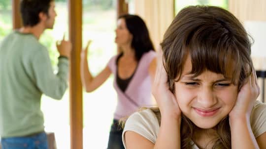 Kind hält sich die Ohren zu, im Hintergrund streitende Eltern