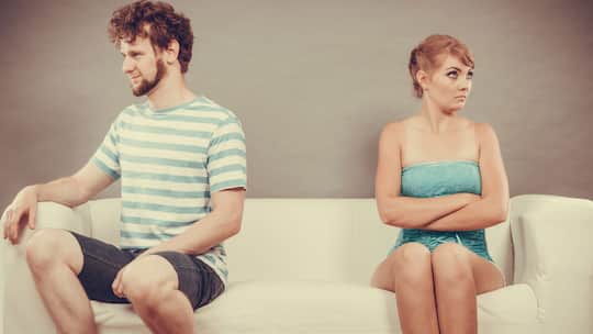 Ein Paar sitzt auf einem Sofa. Beide ignorieren sich gegenseitig.