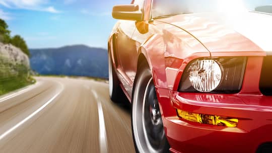 Ein roter Sportwagen fährt auf einer Landstrasse