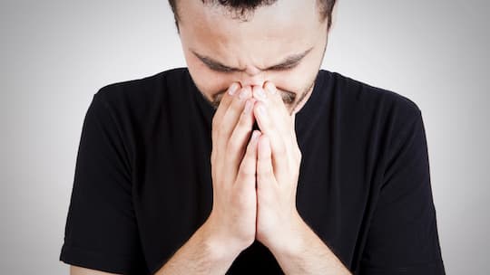 Ein junger Mann, der gesundheitlich angeschlagen wirkt, hält sich die Hände vors Gesicht.