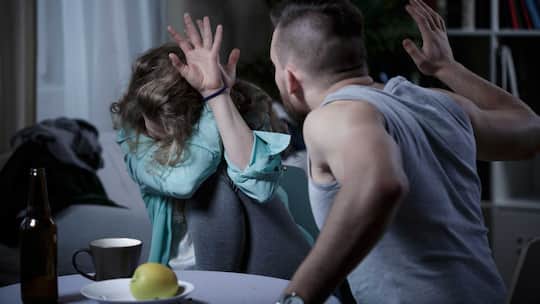 Ein Mann holt zum Schlag auf eine Frau aus. Die gewalttätige Szene spielt sich zu Hause ab.